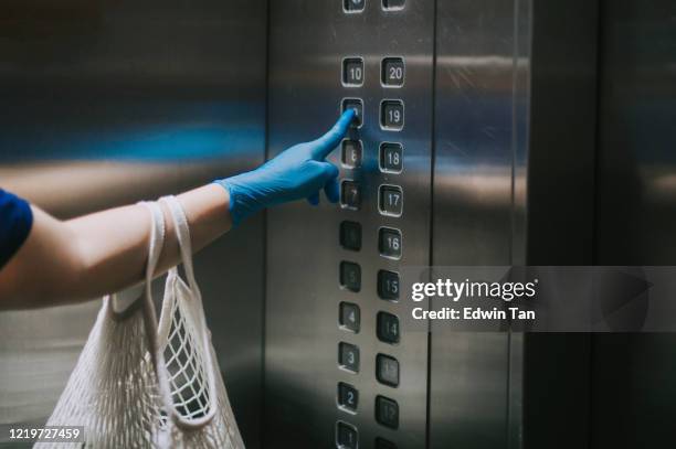an asian chinese woman pressing the lift elevator button with her reusable bags of groceries - social distancing elevator stock pictures, royalty-free photos & images
