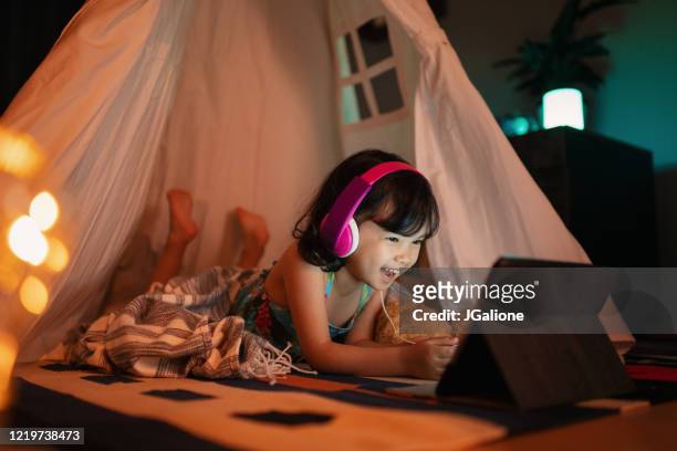 Young girl watching a digital tablet at night whilst relaxing in a tent in her bedroom
