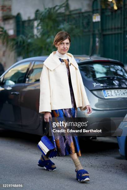 Guest wears a white turtleneck pullover, a white jacket, a blue and purple lustrous dress, a blue and white leather bag, brown socks, blue shoes,...