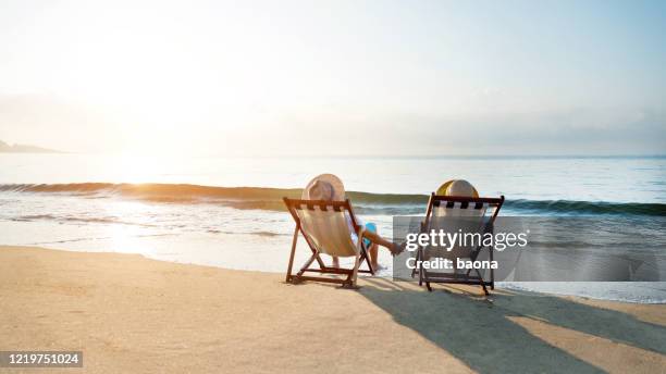 paar sitzt auf liegestuhl am strand - beach deck chairs stock-fotos und bilder