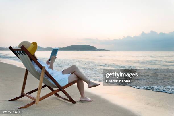 woman using digital tablet at the beach - summer tablet stock pictures, royalty-free photos & images