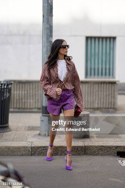Gilda Ambrosio wears sunglasses, a white t-shirt, a red and white striped opened shirt, purple shorts, a red bag, purple pointy shoes, outside Etro,...