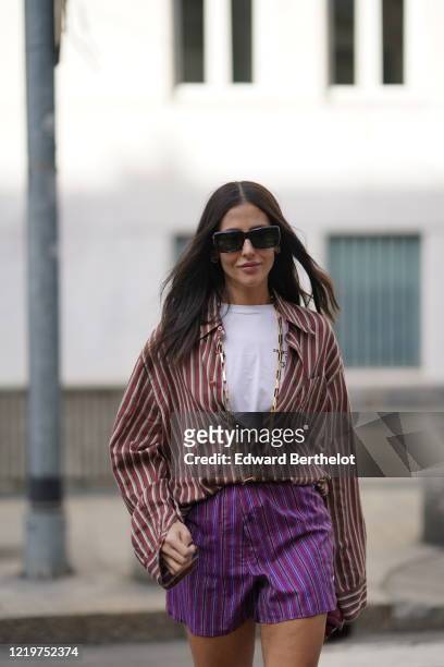 Gilda Ambrosio wears sunglasses, a white t-shirt, a red and white striped opened shirt, purple shorts, a red bag, outside Etro, during Milan Fashion...