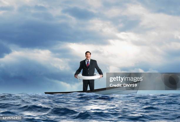 businessman wearing life preserver as boat is about to sink - rowboat stock pictures, royalty-free photos & images