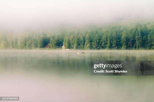 a canoe moves across misty morning lake - brume riviere photos et images de collection