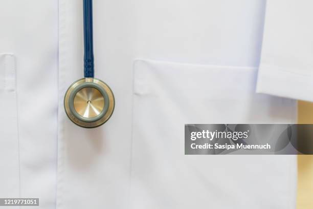 close up of stethoscope and medical lab coat hanging on the wall - doctor lab coat stockfoto's en -beelden