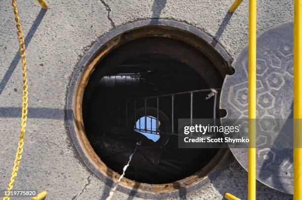 an open manhole on a city street - confined space stock-fotos und bilder
