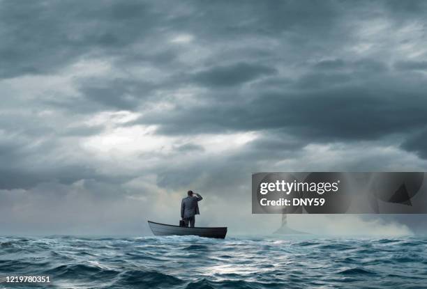 businessman looks at lighthouse while stranded on boat - missing the boat stock pictures, royalty-free photos & images