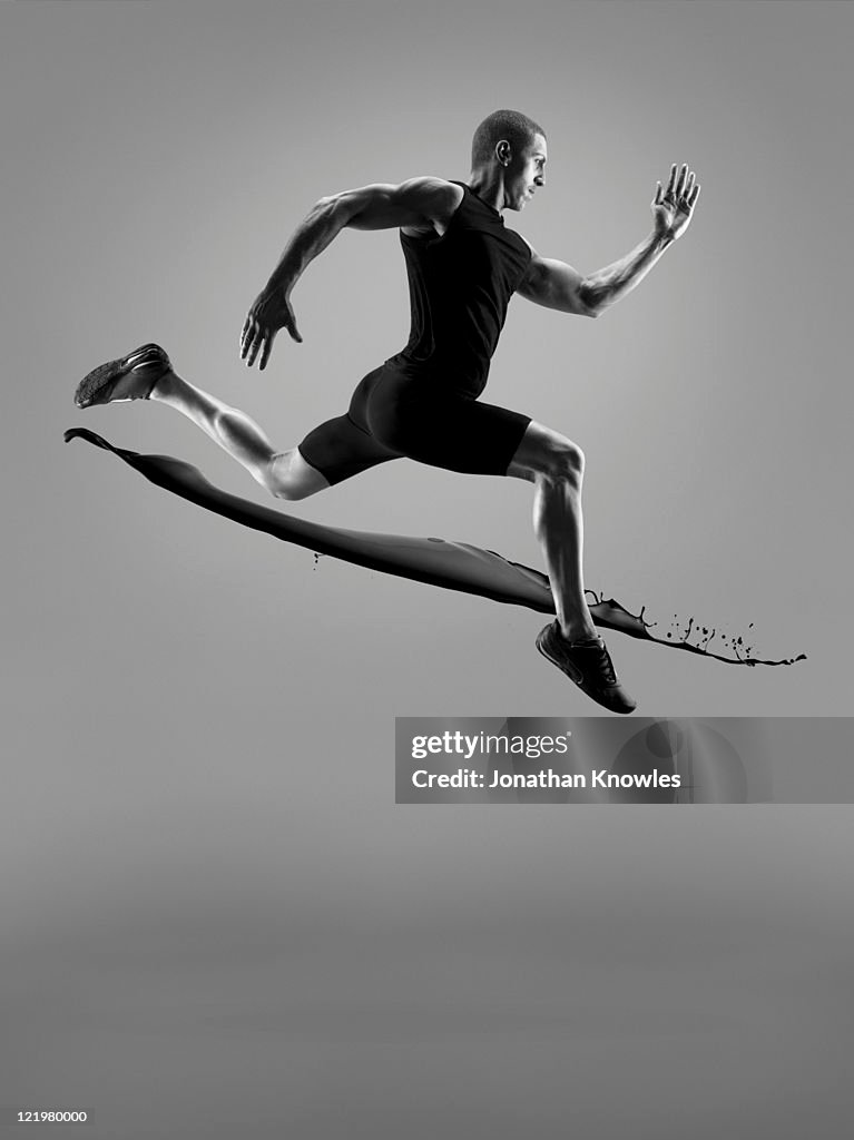 Male athlete running above liquid splash