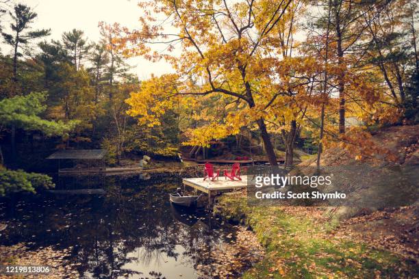 a pair of red chairs on a cottage dock - muskoka stock pictures, royalty-free photos & images
