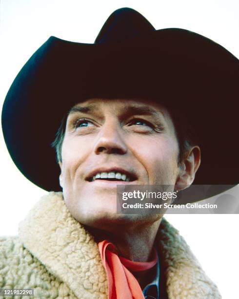 Profile of Jack Lord , US actor, wearing a black cowboy hat and a white fleece jacket with a red neckerchief, circa 1970.