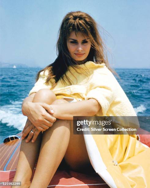 Sophia Loren, Italian actress, wearing a yellow waterproofcoat as she sits on a boat, with surf trailing out on the waters beyond Loren, circa 1965.