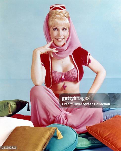 Barbara Eden, US actress, in costume sitting on a multi-coloured pile of cushions in a publicity portrait for the US television series, 'I Dream of...