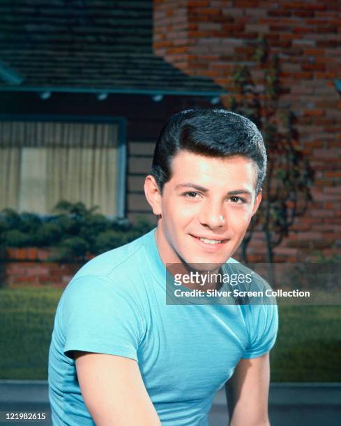 Frankie Avalon, US actor and singer, wearing a blue t-shirt, with a residential property in the background, circa 1960.