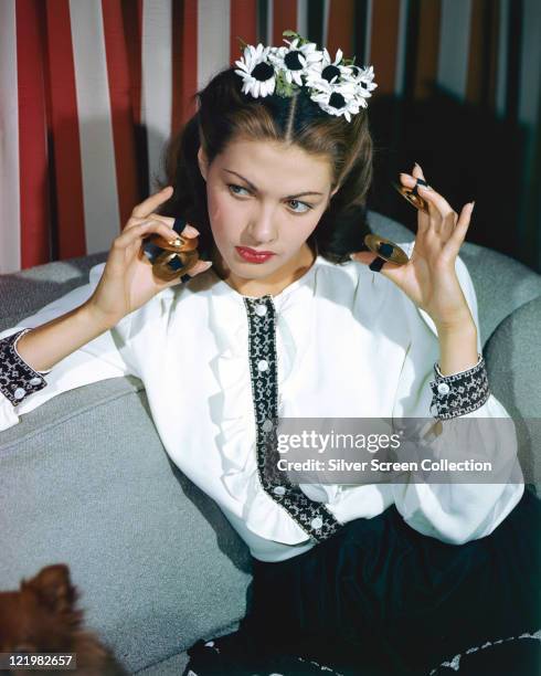 Yvonne De Carlo , Canadian actress, with white flowers in her hair, wearing a white blouse with dark blue trim, with finger cymbals on her fingers,...