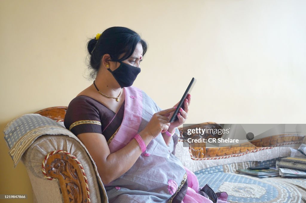 Indian woman with face protective mask reading news on tablet.