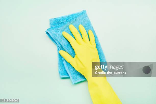 hand in glove with blue cleaning rag on turquoise background - green glove stockfoto's en -beelden