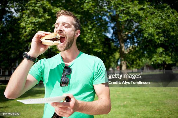 a man enjoying a burger in a city park - burger portrait photos et images de collection