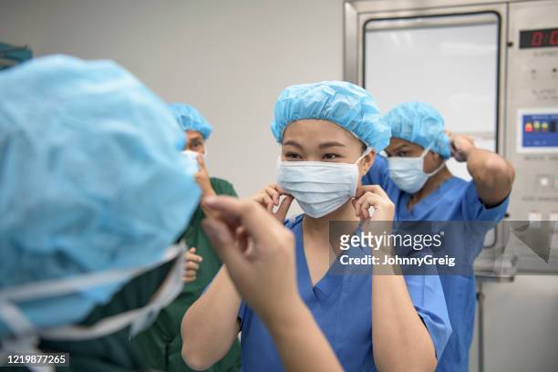 equipe médica masculina e feminina colocando máscaras cirúrgicas - máscara cirúrgica - fotografias e filmes do acervo