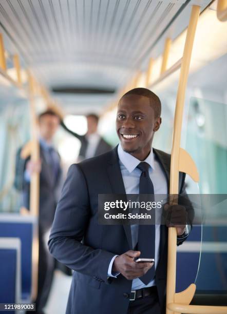 businessman standing in train, holding phone - man riding bus fotografías e imágenes de stock