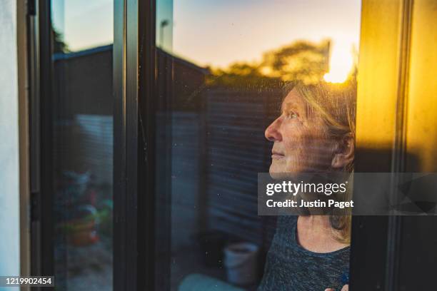 senior woman looking through window - cuarentena fotografías e imágenes de stock