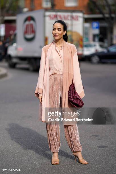 Tamara Kalinic wears a salmon-pink colored flowing long vest, a shirt, pleated lustrous glittering salmon-pink colored pants, a purple leather...