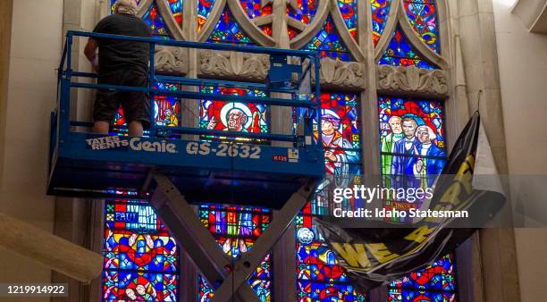 Staff at Cathedral of the Rockies place a "We Repent" banner in front of a stained glass panel depicting Confederate General Robert E. Lee standing...
