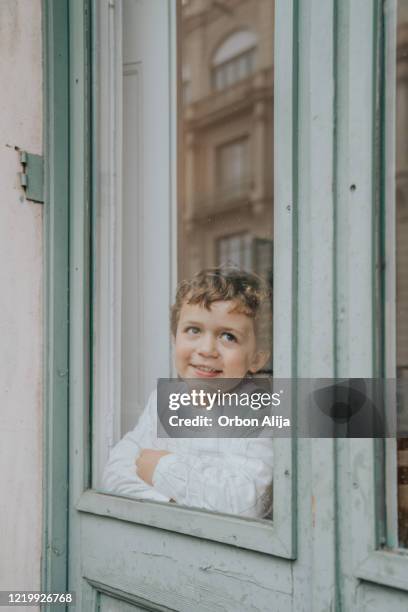 boy in mask sitting near window and looking. stay home concept, coronavirus covid-19 quarantine - coronavirus punishment stock pictures, royalty-free photos & images