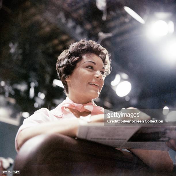 Connie Francis, US singer, wearing a pink neckscarf as she smiles with studio lights in the background, circa 1965.