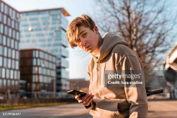 彼のスマートフォンを使用して電動スクーターを持つティーンエイジャー - serious teenager boy ストックフォトと画像