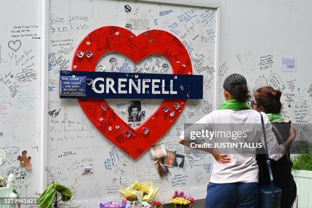 People stand and pay their respects in front of a wall where messages of support have been written, surrounding Grenfell tower in west London on June...