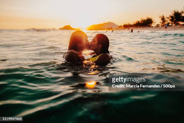 view of two woman swimming and kissing - brazil ocean stock-fotos und bilder