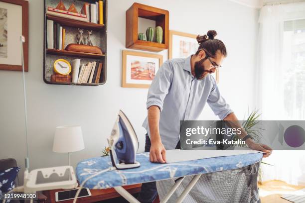 young man ironing his shirt - tábua-de-passar-roupa imagens e fotografias de stock