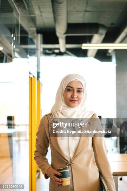 muslim business woman coming to office with laptop and reusable coffe cup. - arabische frau kopftuch stock-fotos und bilder