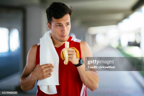 athletic man eating banana after workout outdoors - sportsman stock pictures, royalty-free photos & images