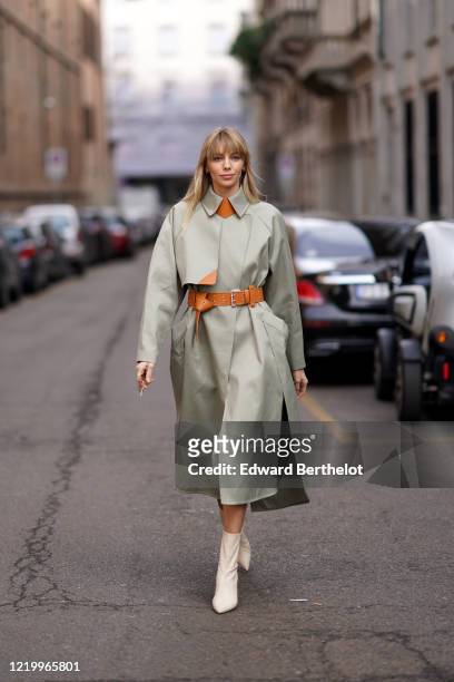 Guest wears a gray trench coat, an brown/orange leather belt, white leather pointy boots, outside Sportmax, during Milan Fashion Week Fall/Winter...