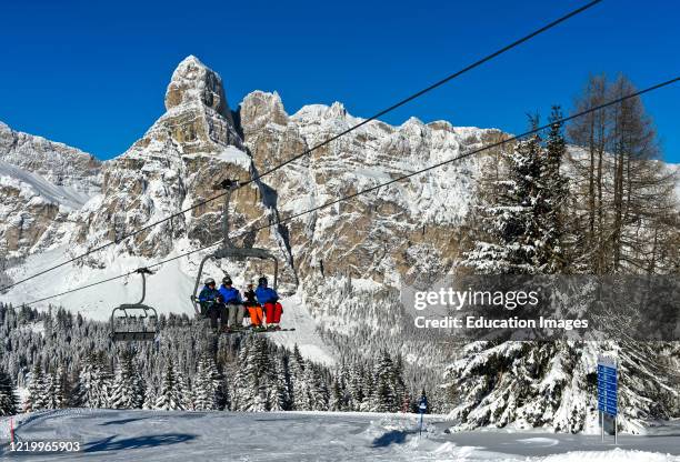Skiers on a chair lift against snow-covered Mount Sassongher, Alta Badia, Dolomites, South Tyrol, Italy.