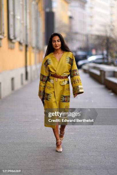 Guest wears a yellow double breasted kimono dress with flared sleeves, a brown leather belt, shoes, outside Etro, during Milan Fashion Week...