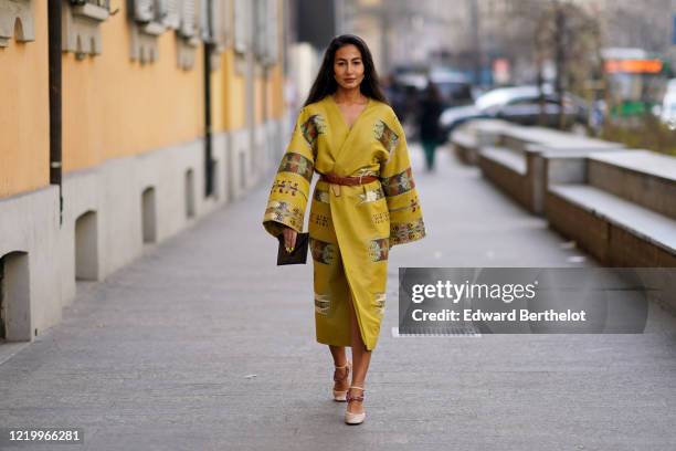 Guest wears a yellow double breasted kimono dress with flared sleeves, a brown leather belt, shoes, outside Etro, during Milan Fashion Week...