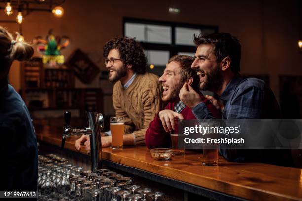 grupo de hombres jóvenes felices bebiendo cerveza y viendo un partido de fútbol en el pub - club soccer fotografías e imágenes de stock