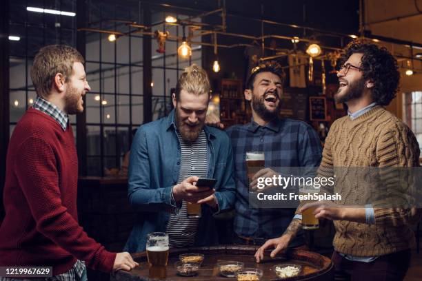 gruppo di uomini che si ridono al pub mentre bevono birra e guardano una partita di calcio sul telefono cellulare - friends drinking foto e immagini stock