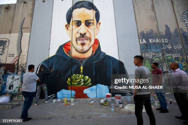 Palestinian men watch artist Taqi Spateen paint a mural of Iyad Hallak, a 32-year-old autistic Palestinian man shot dead by Israeli police, on a...