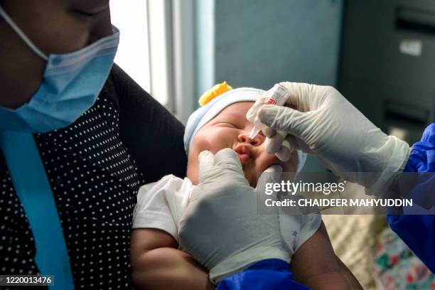 Mother holds her infant as a member of the medical staff clad in protective gear administers the oral vaccine for polio at a community health centre...