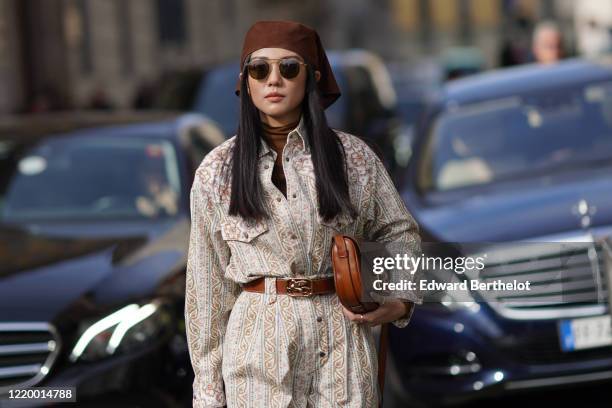 Yoyo Cao wears a brown hat, sunglasses, a jumpsuit, a brown leather belt, a brown leather bag, outside Etro, during Milan Fashion Week Fall/Winter...