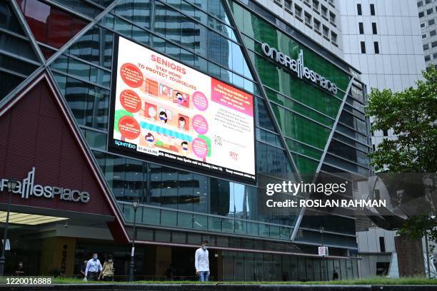 People walk past an electronic board displaying message for seniors to take precaution against the COVID-19 coronavirus at Raffles Place financial...