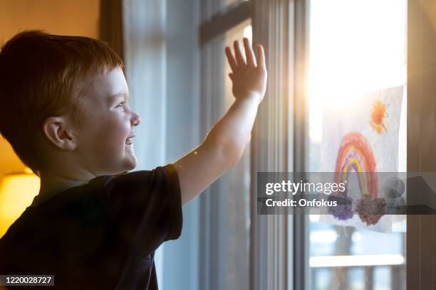 young boy sticking his drawing on home window during the covid-19 crisis at sunset - welcome back phrase imagens e fotografias de stock