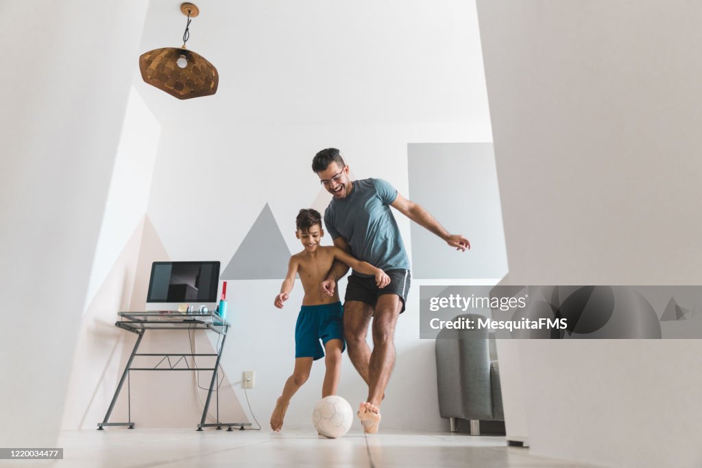 Father and son playing soccer in the living room