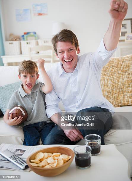 father and son cheering while watching tv - blonde cheering stock-fotos und bilder