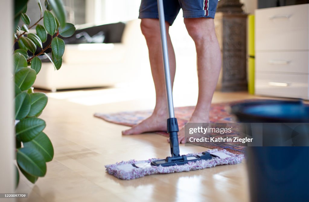 Man cleaning living room floor with mop, low section