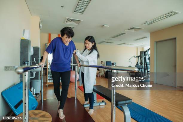 aziatische chinese hogere vrouwen die parallelle staven houden en terwijl fysiotherapeuten die aan kant in een rehabcentrum bij het ziekenhuis helpen - afkickcentrum stockfoto's en -beelden